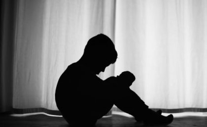 A profile photo in shadow of a young boy seated and looking down dejectedly.